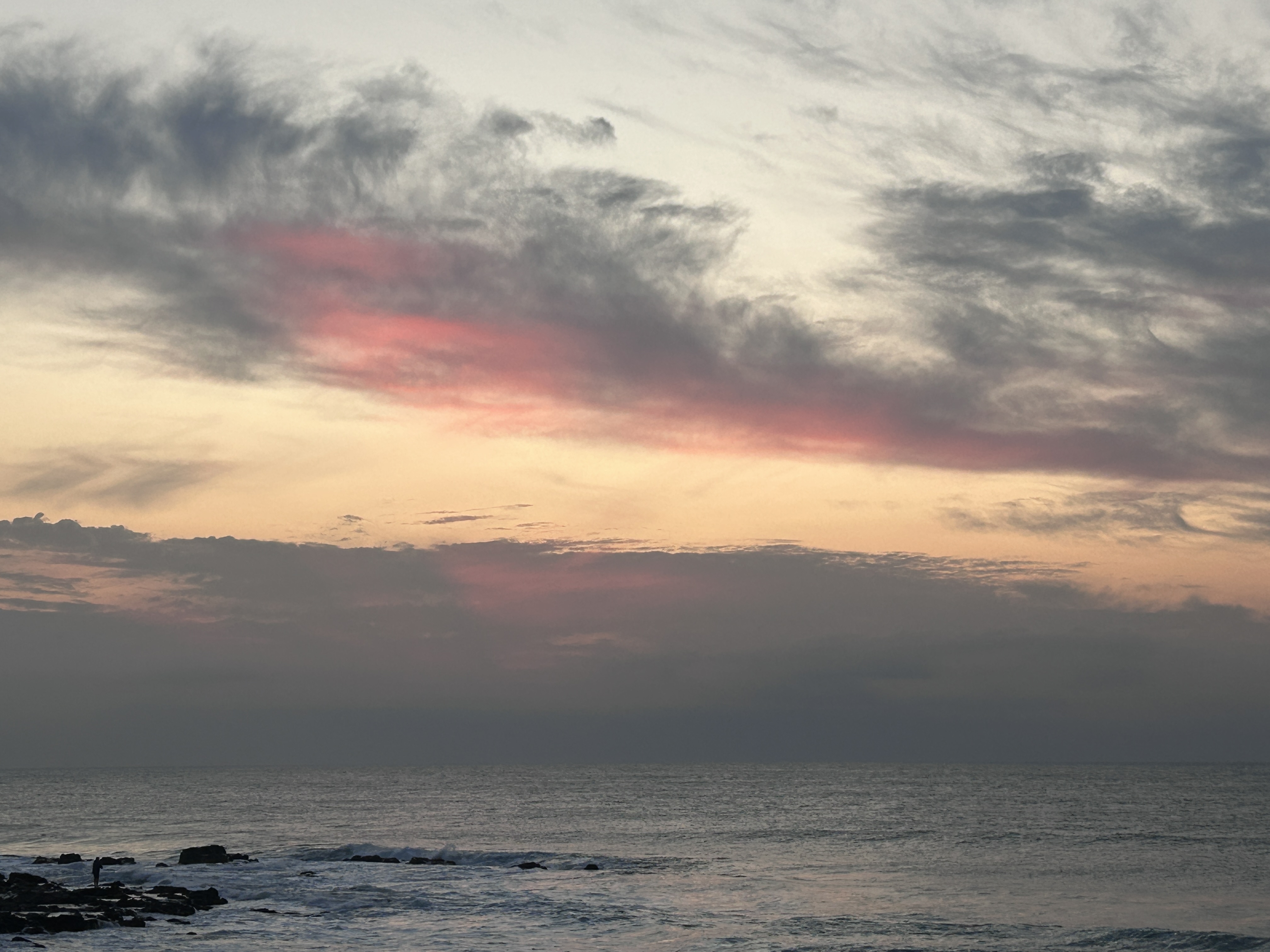 Moody ocean sky at dusk with a lone figure on the rocks